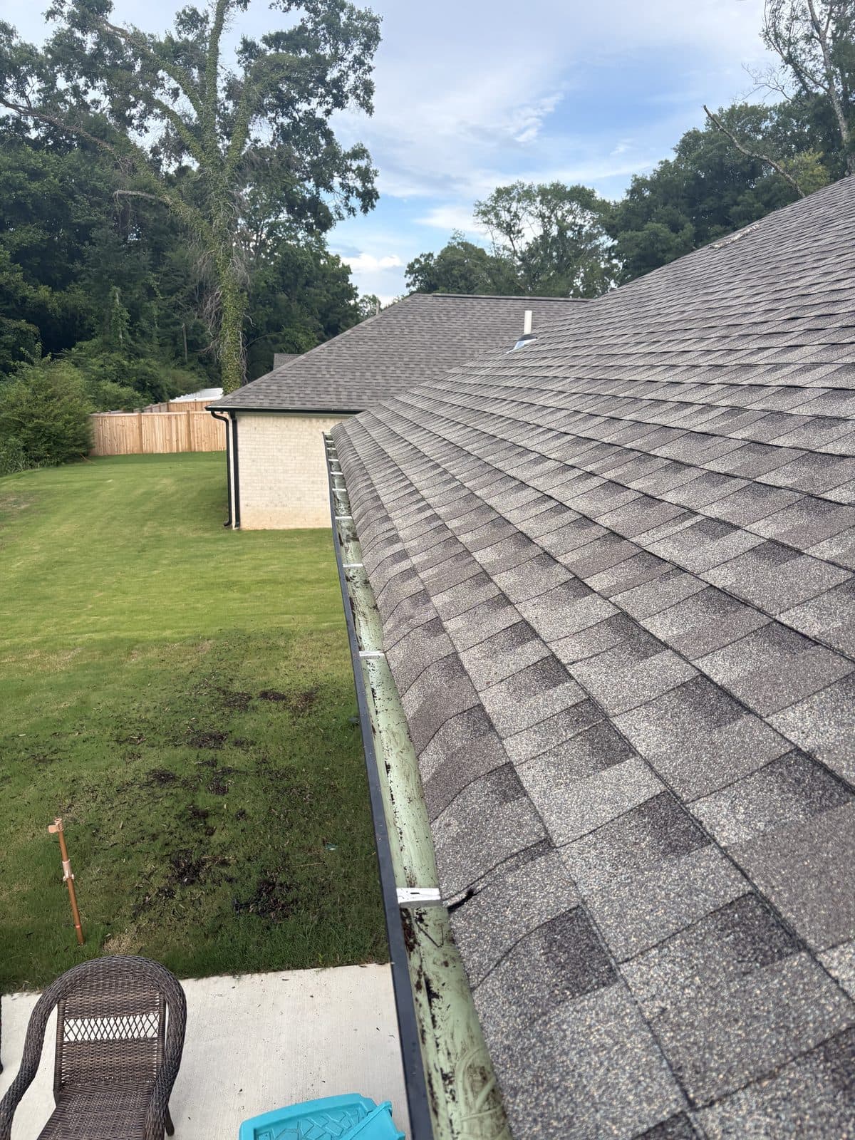 A gutter run packed with leaves and roof grit before cleaning, looking down the roofline
